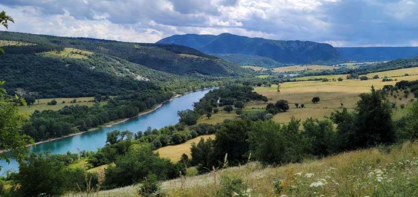 Légifotó egy magyarországi védett tájról: kanyargó folyó zöldellő erdők között, távolban dombokkal és felhős éggel, szemléltetve a természet szépségét és a környezetvédelem fontosságát.